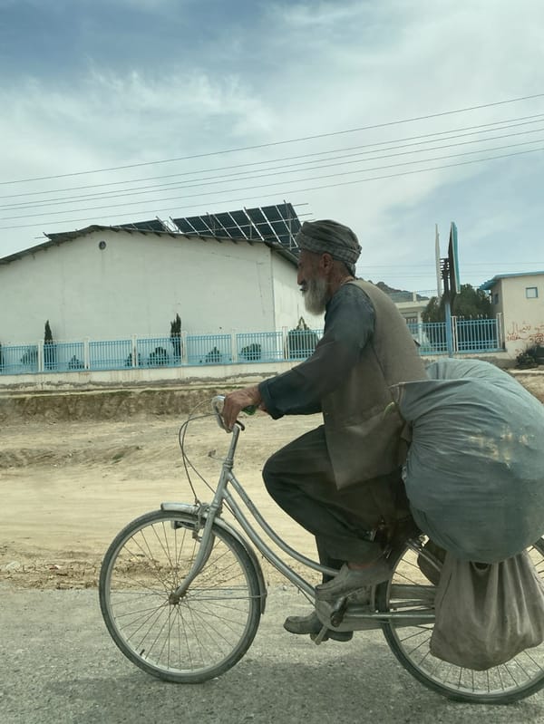 Elderly man rides bicycle on dusty road in Afghanistan