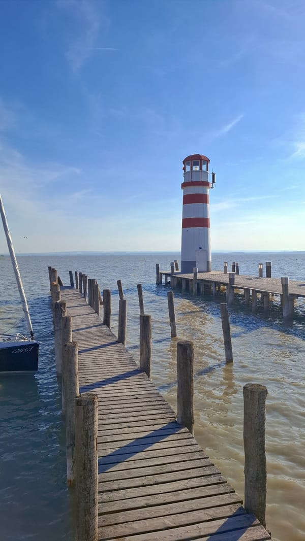 Striped lighthouse observed on wooden pier in Austrian lakeside town
