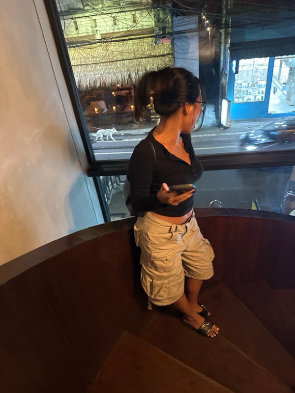 Woman sits by window observing Ubud street scene