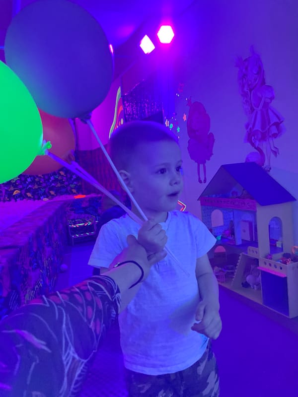 Child plays with balloons, tabby cat rests in colorful indoor space
