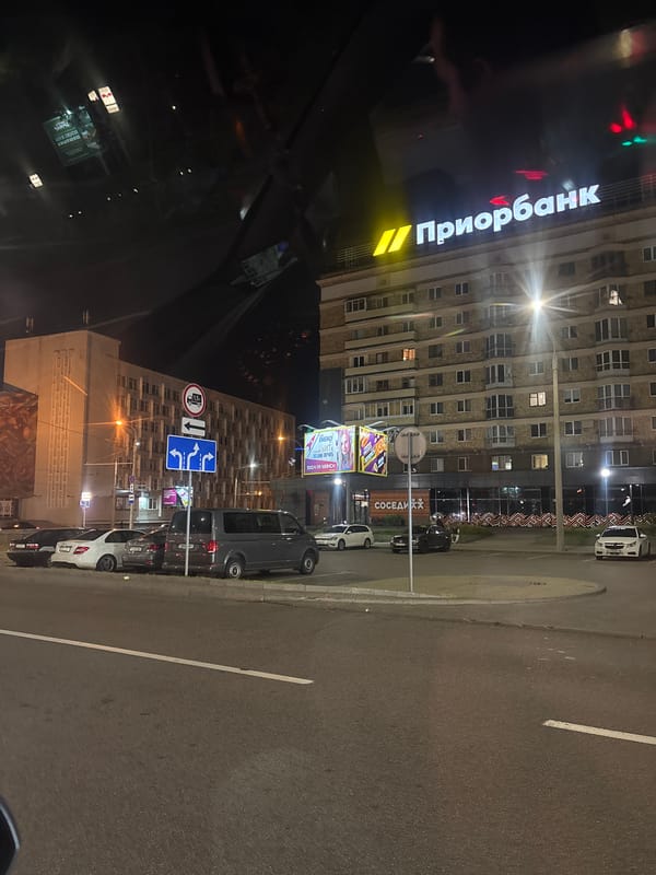 Nighttime street-level drive past a lit Paritetbank building