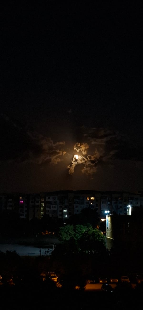 Full moon rises through dramatic clouds over Sofia at night