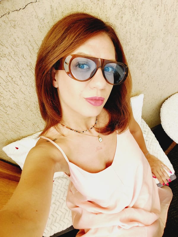 Selfie session against a tan wall, pink dress and sunglasses