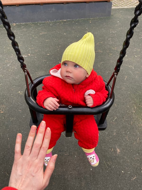 Baby plays in swing at Yekaterinburg playground during spring