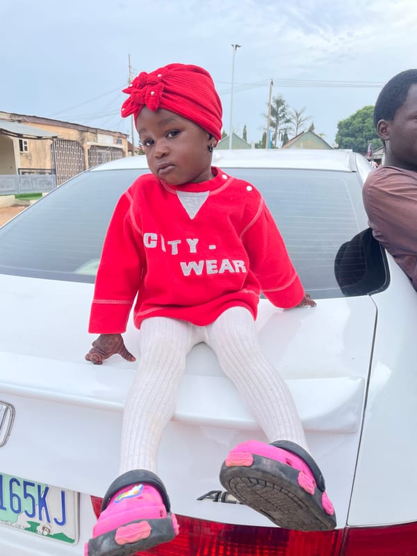 Child in traditional dress sits on car in Nigeria