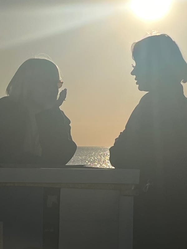 Silhouetted figures gather along sun-drenched coastal breakwater