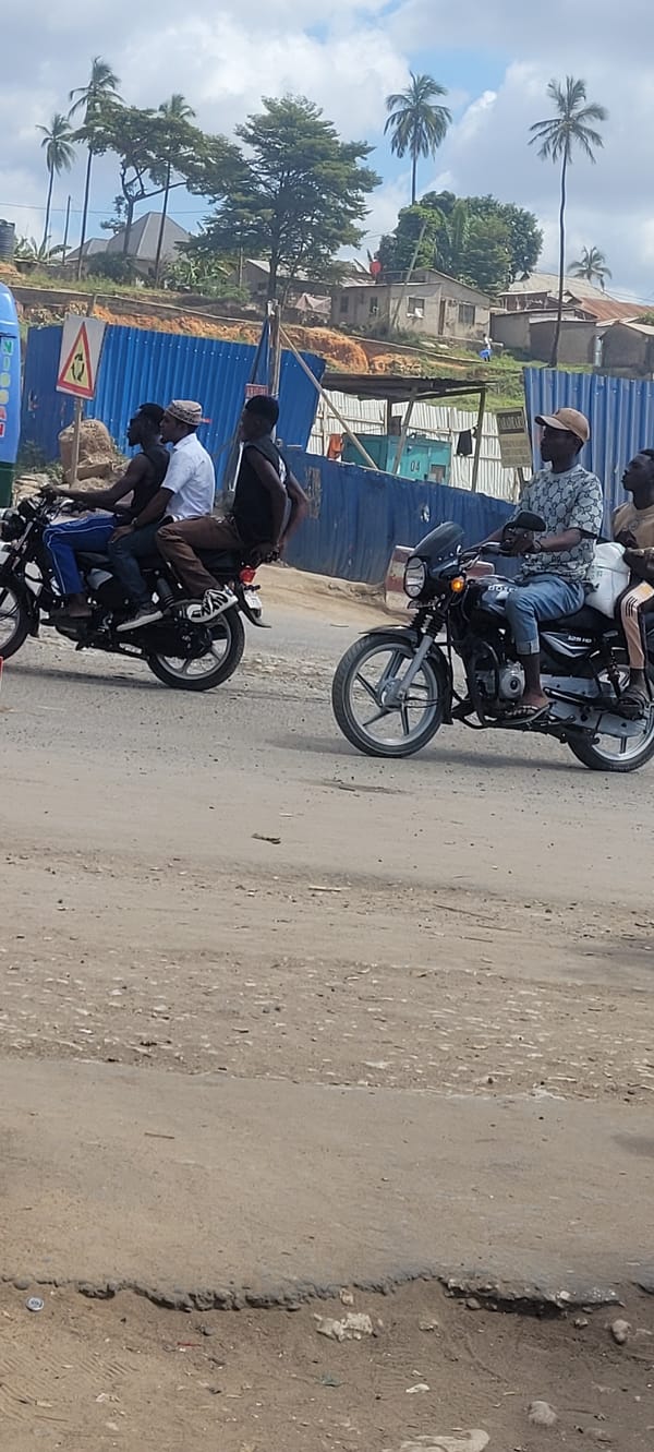 Motorcycles navigate a dusty Dar es Salaam street on a cloudy day