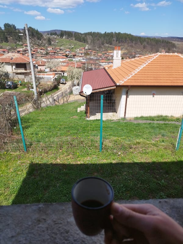 Person enjoys morning coffee overlooking rural landscape from balcony