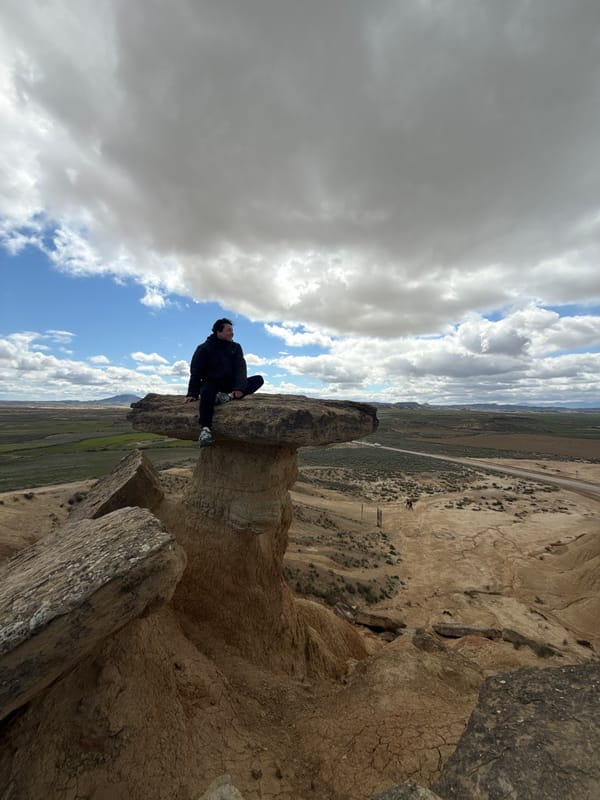 Visitor sits on mushroom rock formation in Bardenas Reales