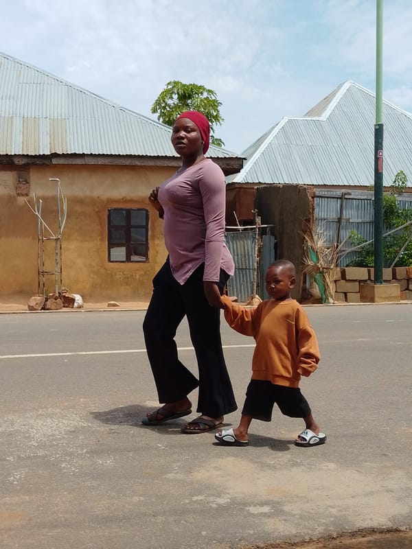 Multiple people on foot along a road near a metal-roofed building