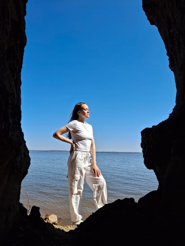 Woman stands at cave entrance overlooking water and sky
