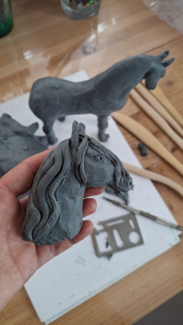 Artist sculpts clay horses in Russian studio, child plays nearby