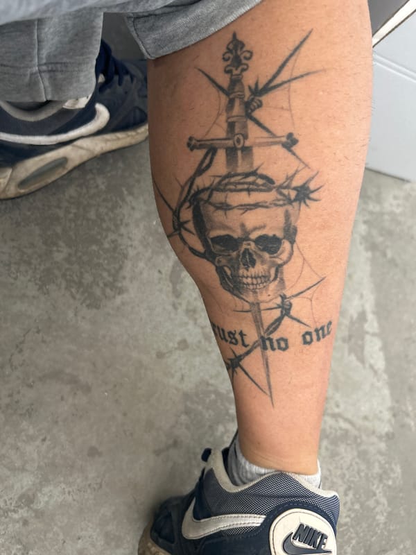 Person displays skull and sword tattoo with "trust no one" text