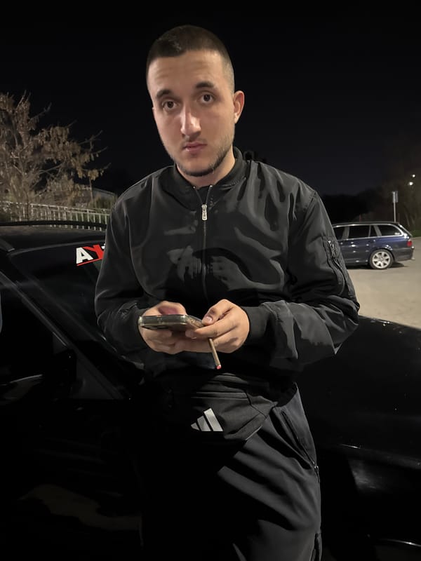 Young man with cigarette and phone leans against car in Topoli
