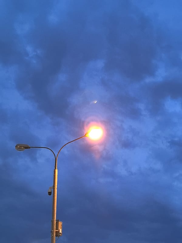 Streetlamp and crescent moon share a cloudy night sky