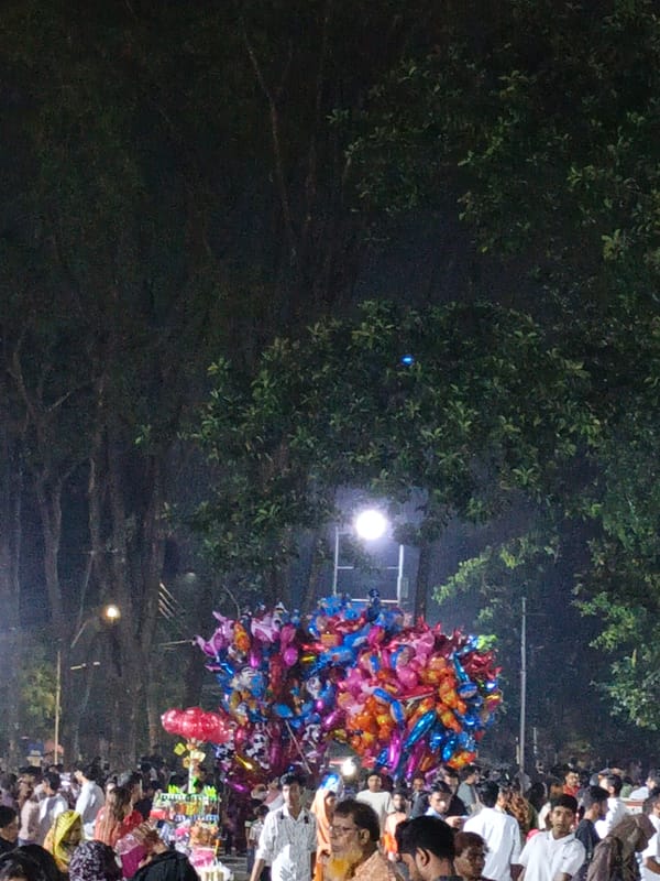 Evening crowd gathers at Dhaka park with balloon vendor