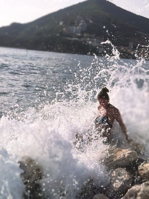 Waves hit a rocky shore near a quiet harbor