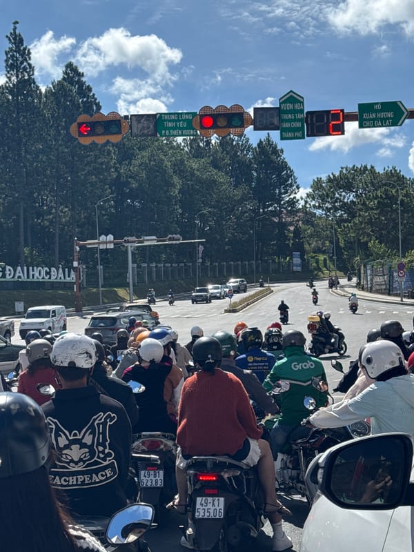 Motorcycles and cars queue at a Đà Lạt intersection on a clear day