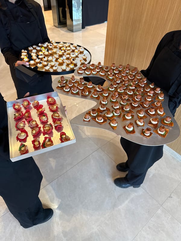Two servers hold appetizer trays on marble floor