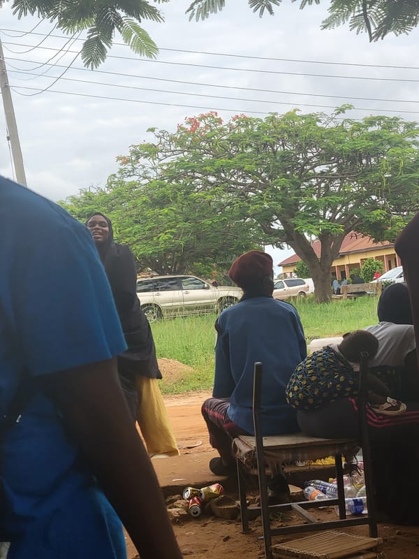 Two people rest outdoors under trees in Keffi