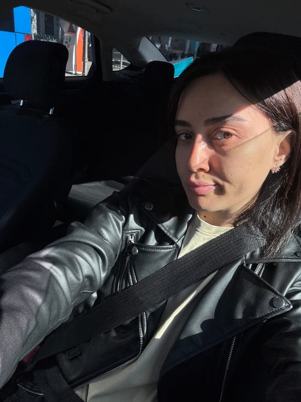 Woman in black jacket seated in car, Tbilisi morning