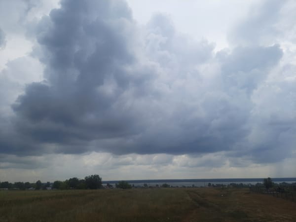 Storm clouds gather over open fields and water near Krestyanka
