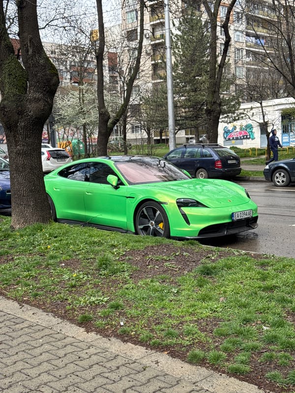Green car parked near sidewalk, person by graffitied building