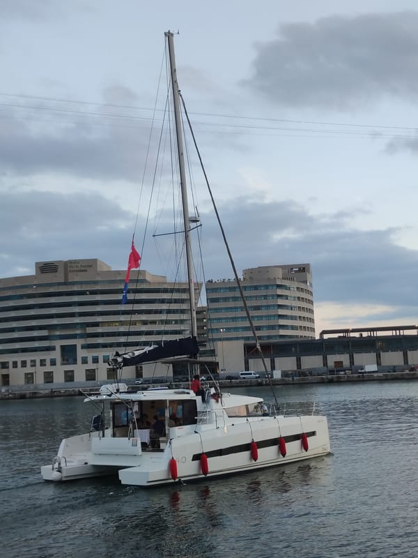White catamaran sails Barcelona harbor at twilight