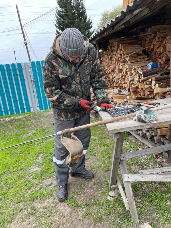 Man repairs weed whacker in outdoor workshop, Talmenka Russia