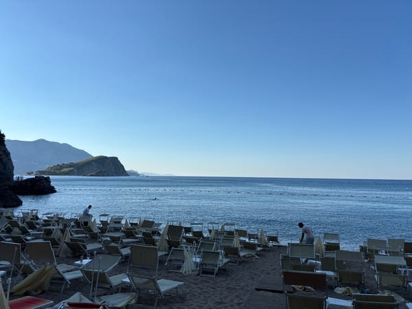 Empty beach chairs face a calm blue ocean with hills beyond