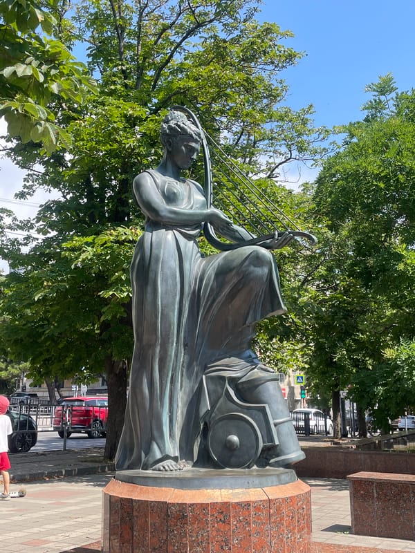 Bronze lyre-playing statue on a red granite pedestal