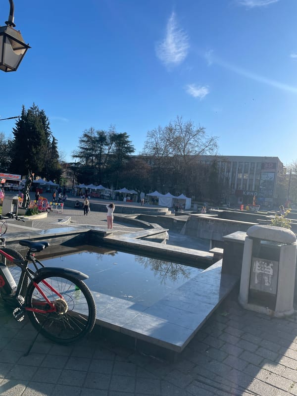 Dog rests in sunny Pazardzhik plaza alongside parked bicycle