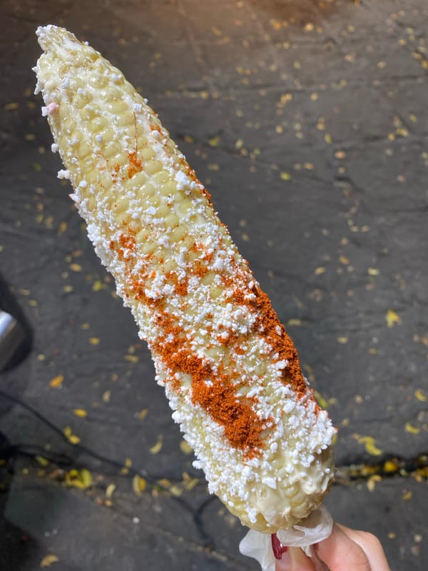 Street corn held over city asphalt with traditional toppings
