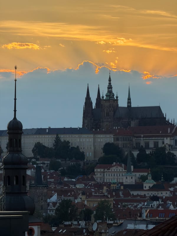 Prague's rooftops glow under a dramatic dusk sky