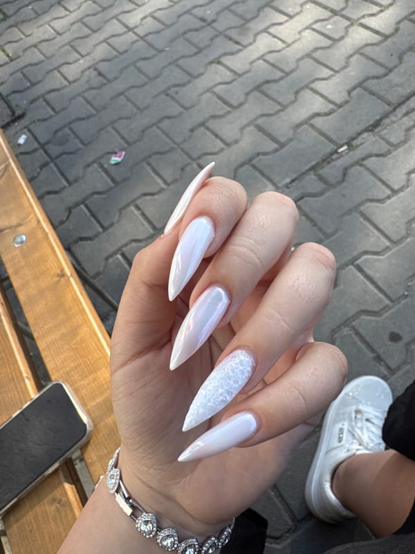 Person displays elaborate white stiletto nails with glitter finish