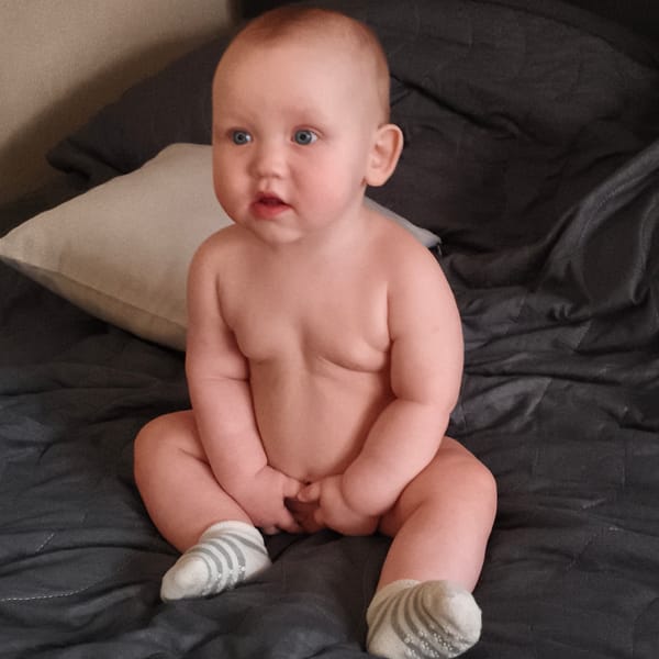 Baby observed sitting on gray blanket wearing striped socks