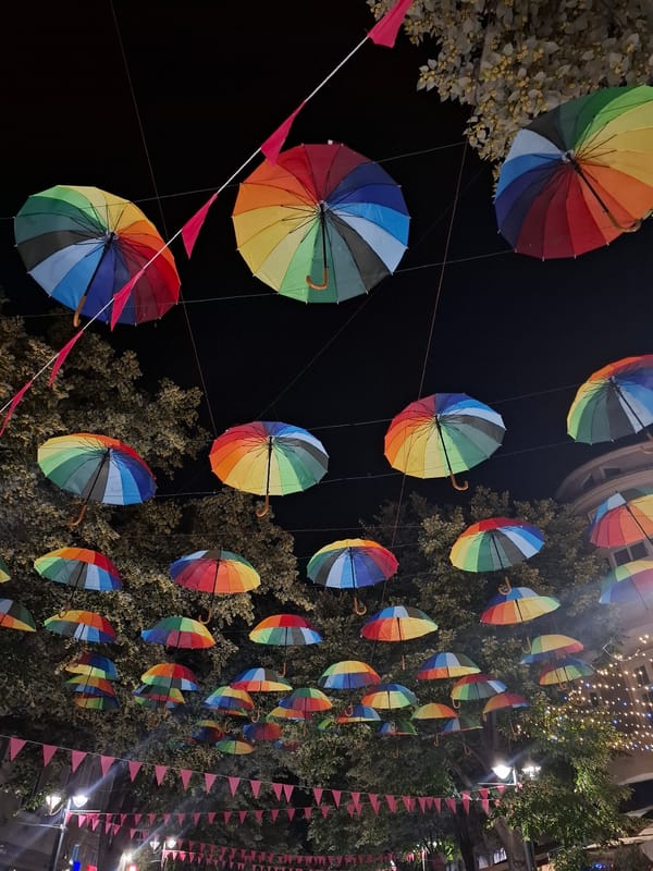 Rainbow umbrellas hang over a lit-up street at night