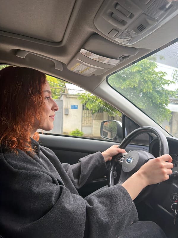 Woman drives Subaru through green hills of Tbilisi morning