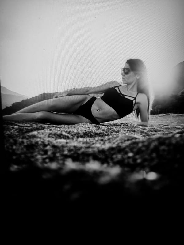 Posing on a rocky beach in a black bikini and sunglasses