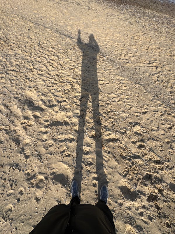 Beach walker's shadow captured on shell-scattered East Suffolk shore
