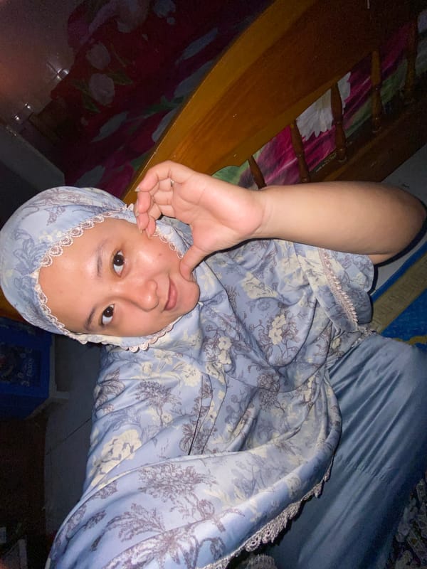 Person in blue headscarf rests on bed in Gelam