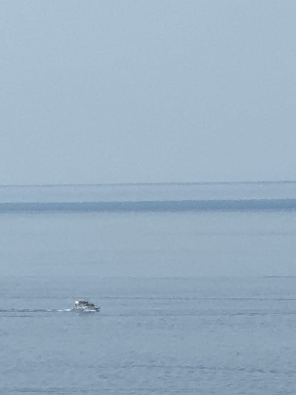 Small boat cuts through hazy morning waters off Boreti