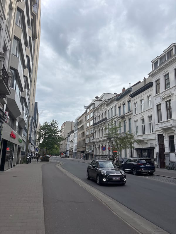 Person in leather jacket walks past parked Vespa in Antwerp