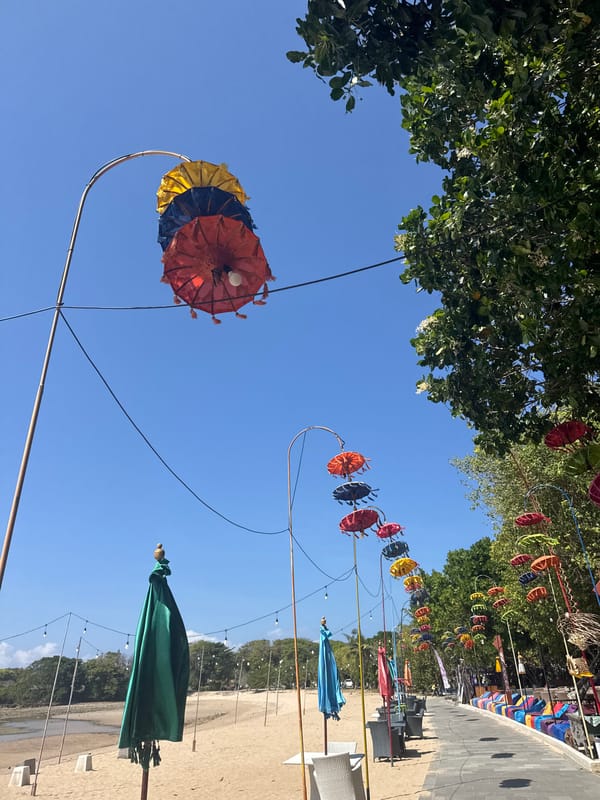 Colorful beachside promenade with kites, cyclists, and decorative umbrellas