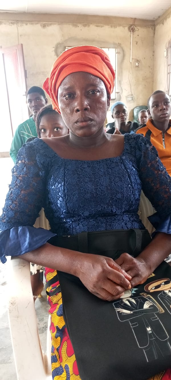 Woman in orange headwrap sits quietly in Lokoja