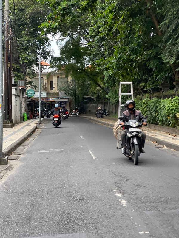 Motorcyclist carries metal frame through Kuta street traffic