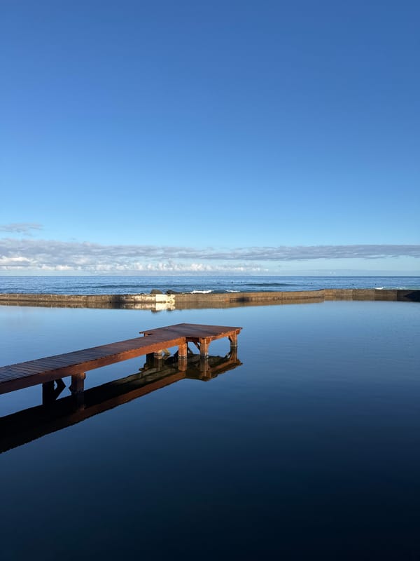 Tenerife coastline: pier, tidal pool, and surfers on a calm morning