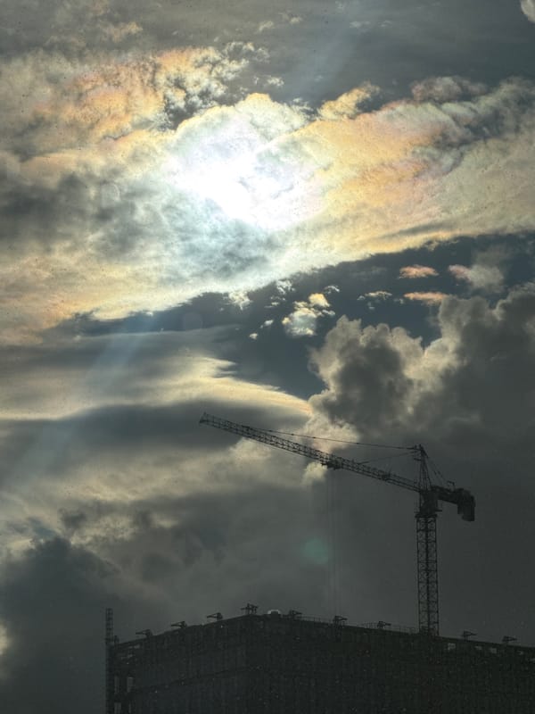 Rain moves through a city, cranes and umbrellas in the mix