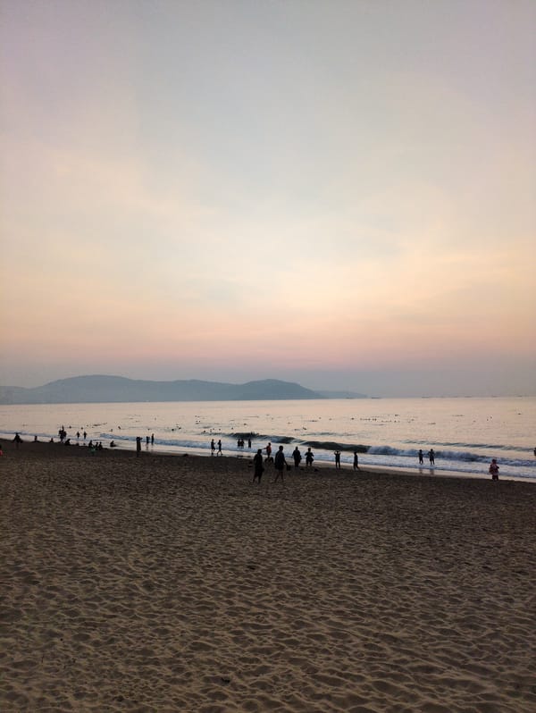 Beach sunset displays peach sky with distant mountains