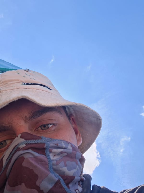 Masked individual photographed against blue sky in selfie